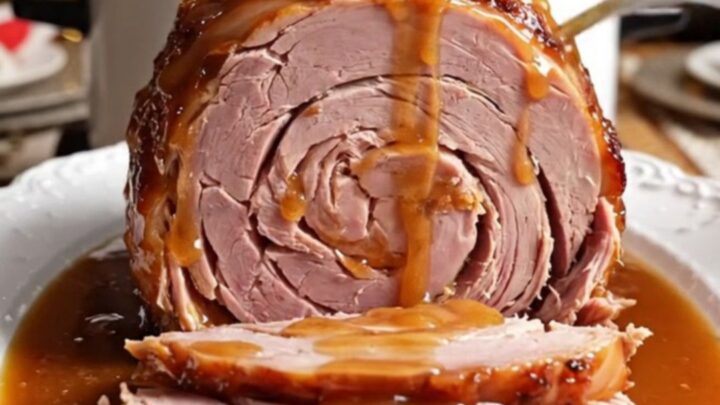 A glistening spiral-sliced ham in a white ceramic crockpot topped with pineapple rings and cherries.