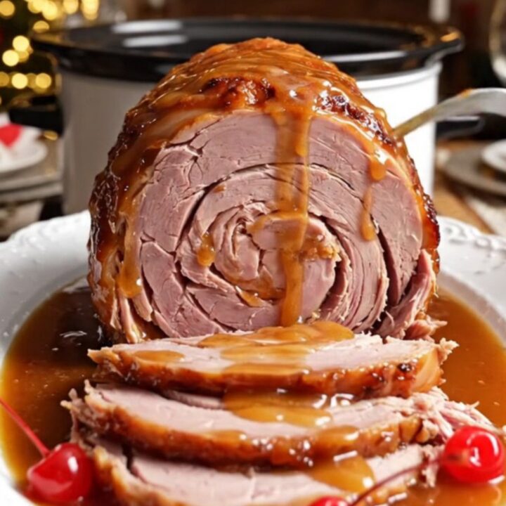 A glistening spiral-sliced ham in a white ceramic crockpot topped with pineapple rings and cherries.