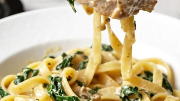 A plate of creamy Tuscan pork chops served over a bed of fettuccine with visible sun-dried tomatoes and spinach.
