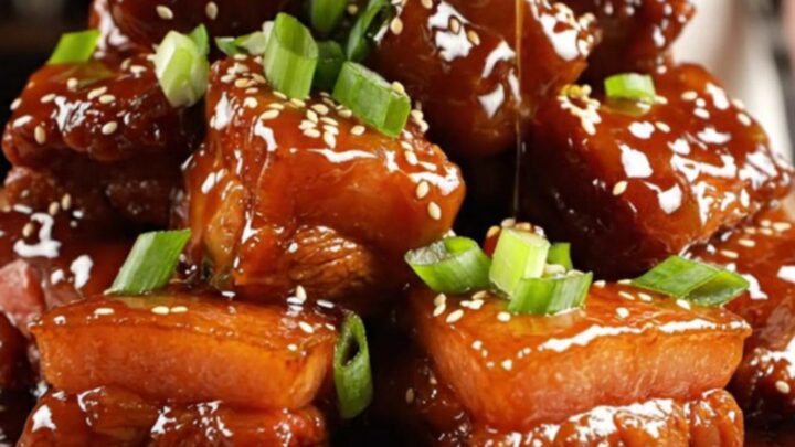 A close-up shot of caramelized, sticky honey garlic pork belly burnt ends served on a wooden board.