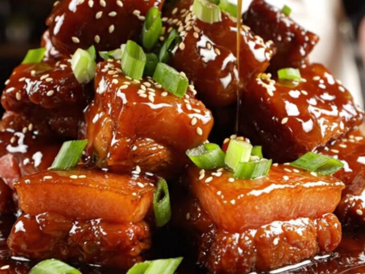 A close-up shot of caramelized, sticky honey garlic pork belly burnt ends served on a wooden board.