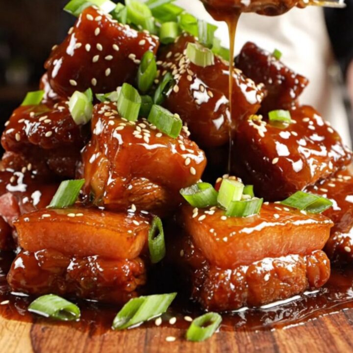 A close-up shot of caramelized, sticky honey garlic pork belly burnt ends served on a wooden board.