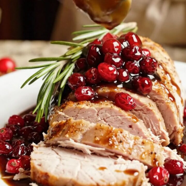 A close-up of sliced pork tenderloin topped with a glossy, ruby-red balsamic cranberry compote on a white platter.