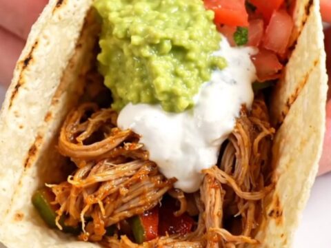 A red ceramic slow cooker filled with smoky chipotle-lime pork tenderloin strips, colorful bell peppers, and red onions.