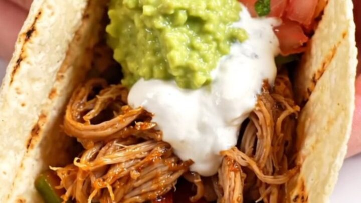 A red ceramic slow cooker filled with smoky chipotle-lime pork tenderloin strips, colorful bell peppers, and red onions.