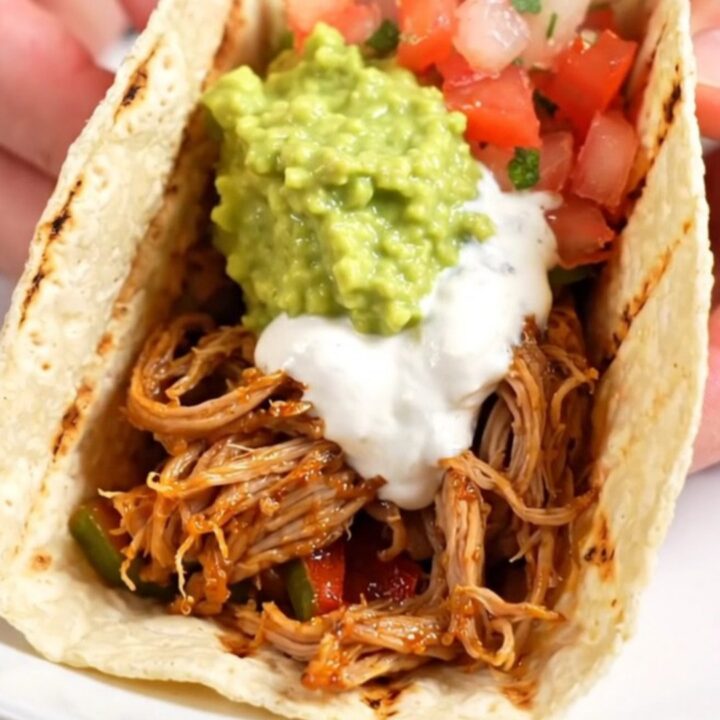 A red ceramic slow cooker filled with smoky chipotle-lime pork tenderloin strips, colorful bell peppers, and red onions.