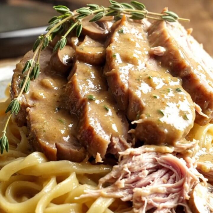 A rustic stoneware slow cooker filled with creamy mushroom gravy and tender sliced pork loin.