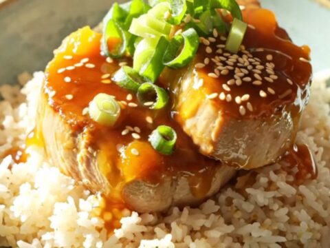 A white ceramic slow cooker filled with sliced, golden-glazed pork tenderloin medallions.