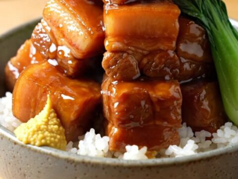 A close-up shot of glossy, braised pork belly cubes in a dark soy glaze inside a matte-black slow cooker.