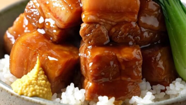 A close-up shot of glossy, braised pork belly cubes in a dark soy glaze inside a matte-black slow cooker.
