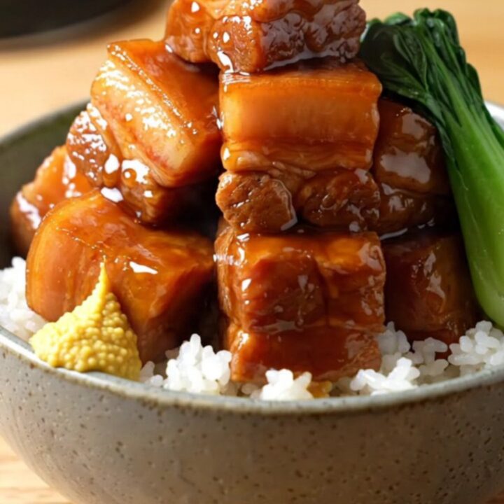 A close-up shot of glossy, braised pork belly cubes in a dark soy glaze inside a matte-black slow cooker.