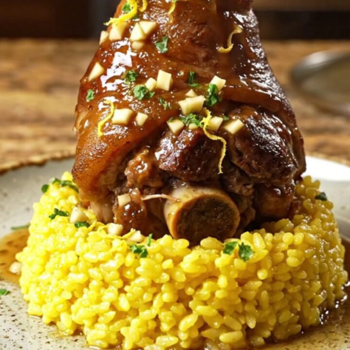 A towering braised pork shank served over creamy saffron risotto with a vibrant lemon-garlic-parsley gremolata.