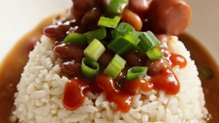 A close-up of a dark stoneware slow cooker filled with creamy red kidney beans, sliced Andouille sausage, and ham.