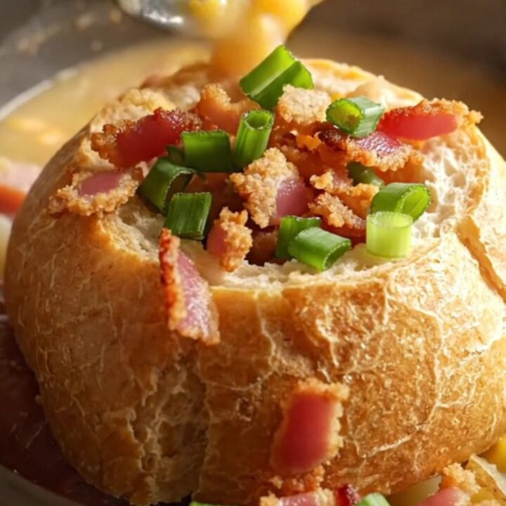 A close-up of a creamy chowder in a bread bowl, topped with bacon bits and green onions.
