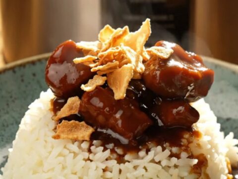 A bowl of glossy Filipino Pork Adobo served over steaming white jasmine rice, topped with golden crispy garlic chips.