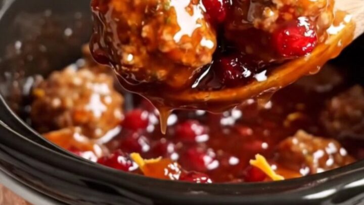 A festive display of juicy pork meatballs in a copper Crockpot, glazed in a vibrant red cranberry-orange sauce.