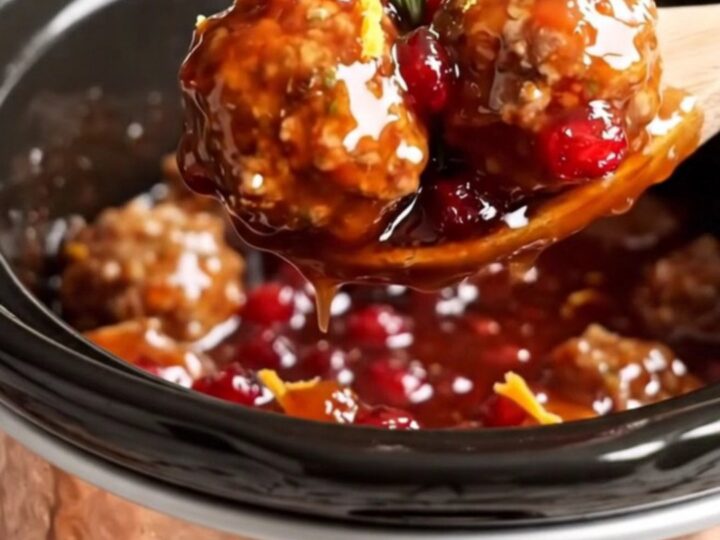 A festive display of juicy pork meatballs in a copper Crockpot, glazed in a vibrant red cranberry-orange sauce.