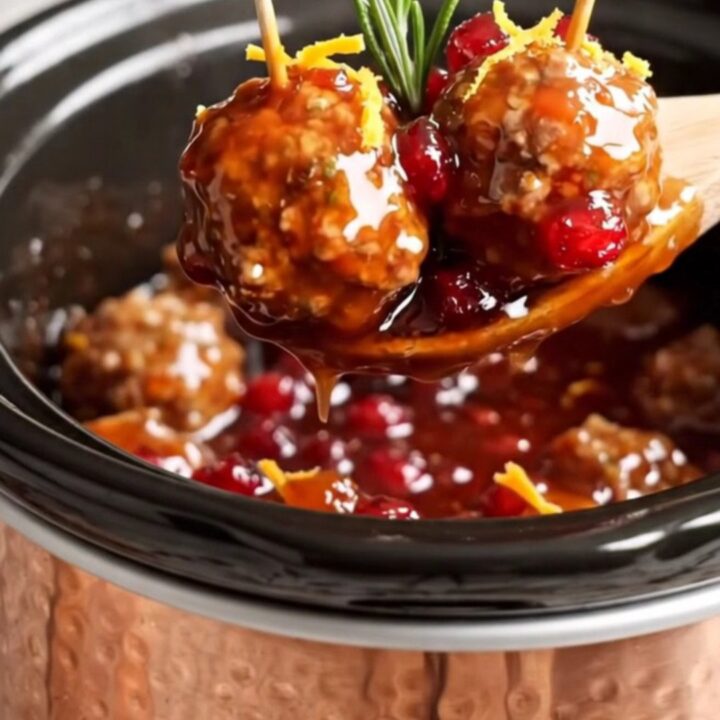 A festive display of juicy pork meatballs in a copper Crockpot, glazed in a vibrant red cranberry-orange sauce.