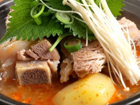 A steaming stone bowl filled with rich, spicy Korean pork bone soup, topped with fresh green onions and perilla leaves.