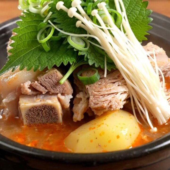 A steaming stone bowl filled with rich, spicy Korean pork bone soup, topped with fresh green onions and perilla leaves.