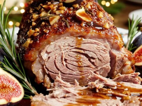 A festive rack of pork with a dark, caramelized fig and rosemary glaze served on a white platter.