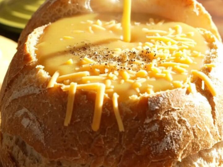 A warm, creamy broccoli cheddar soup served in a hollowed-out sourdough bread bowl on a rustic wooden table.