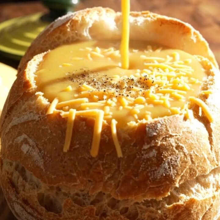 A warm, creamy broccoli cheddar soup served in a hollowed-out sourdough bread bowl on a rustic wooden table.