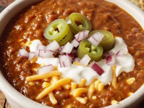 A close-up of a bowl of rich mahogany Texas brisket chili topped with sour cream and jalapenos.