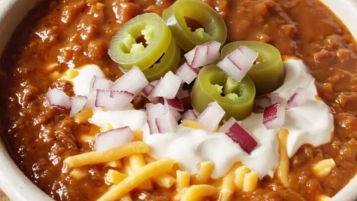 A close-up of a bowl of rich mahogany Texas brisket chili topped with sour cream and jalapenos.