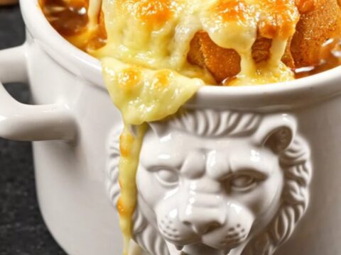 A ceramic crock filled with rich French onion soup, topped with a bubbling, golden brown layer of melted Gruyere cheese.