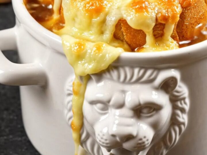 A ceramic crock filled with rich French onion soup, topped with a bubbling, golden brown layer of melted Gruyere cheese.