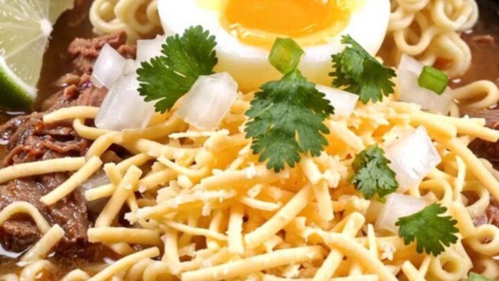 A deep black bowl filled with slow-cooker beef birria ramen, topped with a soft-boiled egg, fresh cilantro, and a lime wedge.