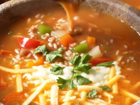 A steaming bowl of stuffed pepper soup topped with melted cheese and fresh parsley.