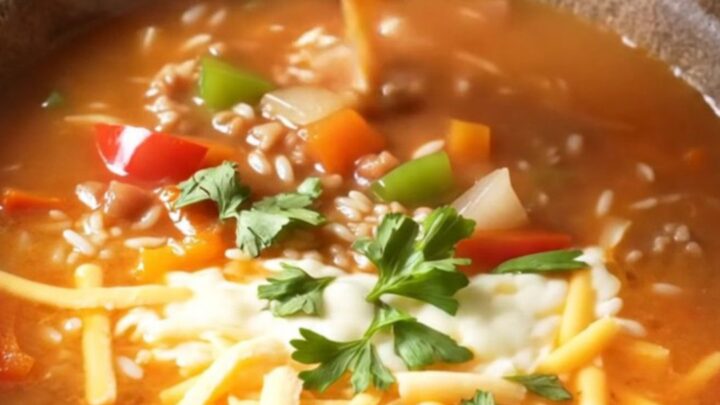 A steaming bowl of stuffed pepper soup topped with melted cheese and fresh parsley.
