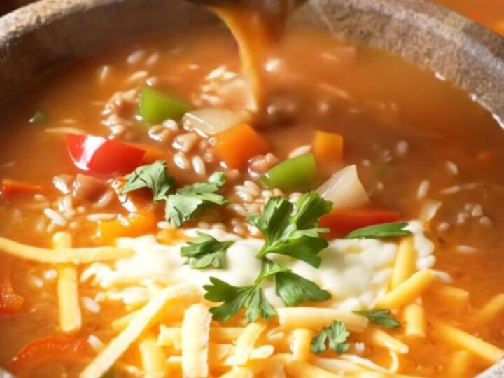 A steaming bowl of stuffed pepper soup topped with melted cheese and fresh parsley.
