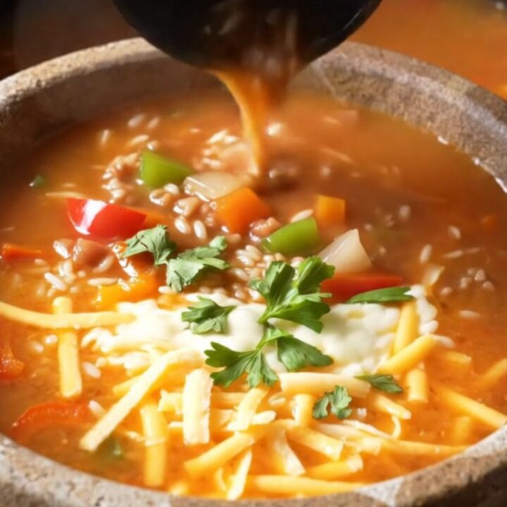 A steaming bowl of stuffed pepper soup topped with melted cheese and fresh parsley.