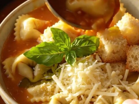A close-up of creamy tomato basil tortellini soup in a ceramic bowl, garnished with croutons and fresh basil.