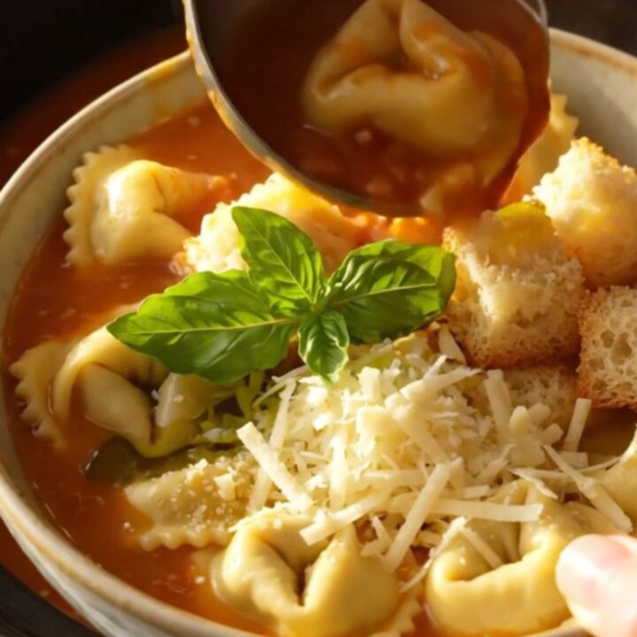 A close-up of creamy tomato basil tortellini soup in a ceramic bowl, garnished with croutons and fresh basil.