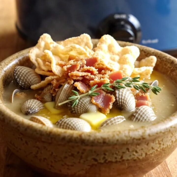 A steaming bowl of creamy New England clam and corn chowder topped with oyster crackers, bacon, and fresh thyme.