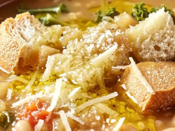 A rustic earthenware bowl filled with thick Tuscan ribollita, topped with a drizzle of olive oil and grated cheese.