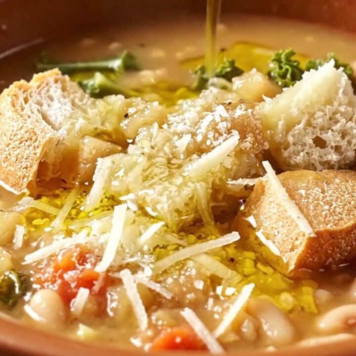 A rustic earthenware bowl filled with thick Tuscan ribollita, topped with a drizzle of olive oil and grated cheese.