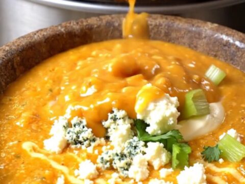 A warm stoneware bowl filled with creamy orange buffalo chicken chowder, topped with blue cheese and celery leaves.