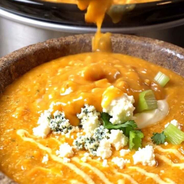 A warm stoneware bowl filled with creamy orange buffalo chicken chowder, topped with blue cheese and celery leaves.