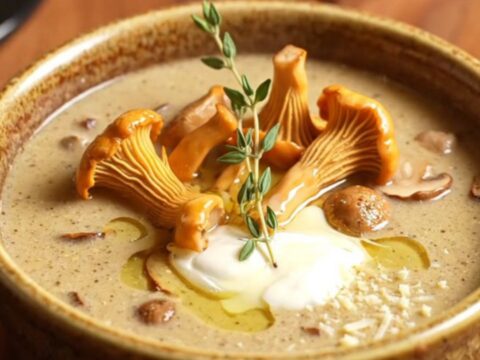 A bowl of velvety wild mushroom soup topped with sautéed chanterelles and thyme in a bistro setting.