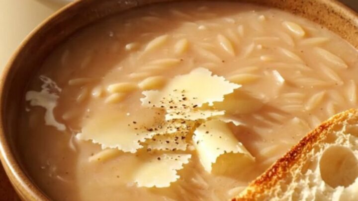 A warm bowl of creamy Tuscan chicken orzo soup topped with Parmesan curls and cracked pepper.