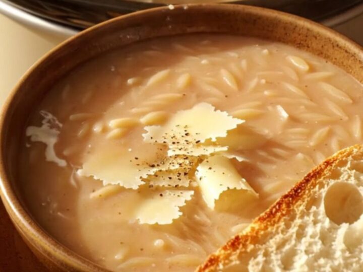 A warm bowl of creamy Tuscan chicken orzo soup topped with Parmesan curls and cracked pepper.