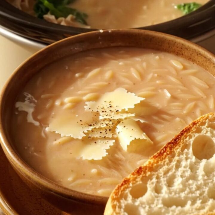 A warm bowl of creamy Tuscan chicken orzo soup topped with Parmesan curls and cracked pepper.