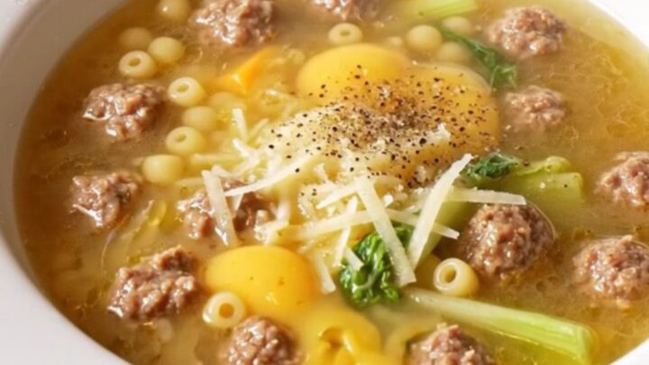 A wide rimmed bowl filled with Italian wedding soup featuring mini meatballs, pearl pasta, and escarole.