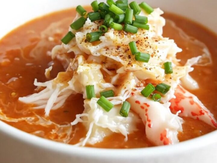 A warm, creamy roasted red pepper bisque served in a white porcelain bowl, topped with jumbo lump crab and chives.