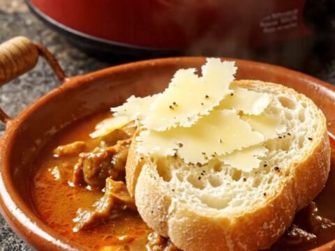 A rustic terracotta cazuela bowl filled with smoky chorizo and chickpea stew topped with Manchego cheese.